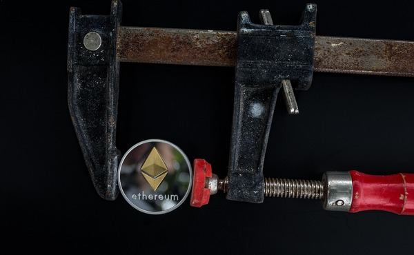 Ethereum coin pressed in a red metal clamp
