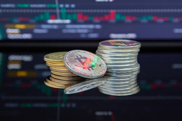 Stacks of gold and silver crypto coins in front of trading charts