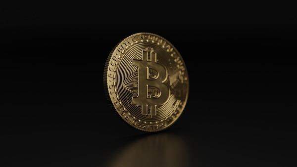 Single gold Bitcoin coin standing on a dark surface