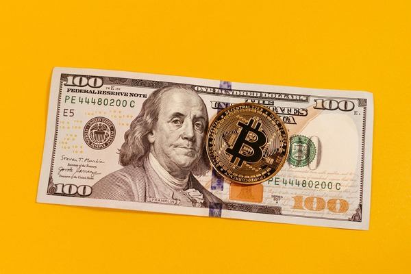 Bitcoin coin on a 100 dollar bill against a yellow background