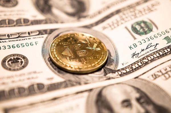 Gold Bitcoin coin resting on US dollar banknotes